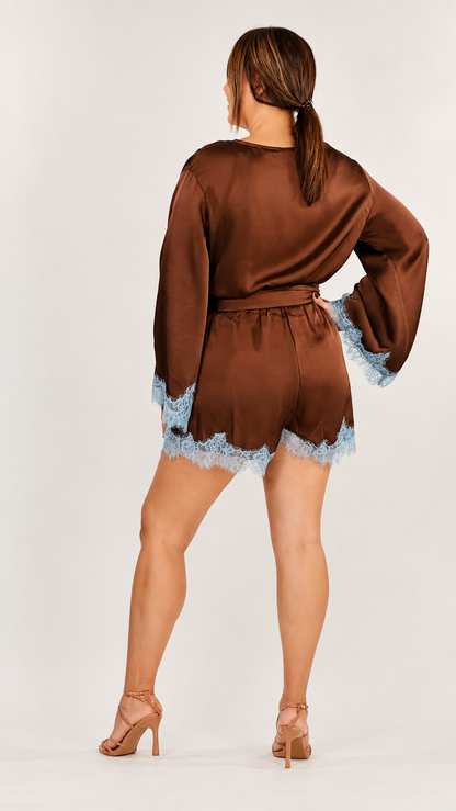 Romper corto de mujer color chocolate con acabado satinado, escote cruzado, mangas largas con encaje azul claro, cintura con lazo y ruedo decorado con encaje.