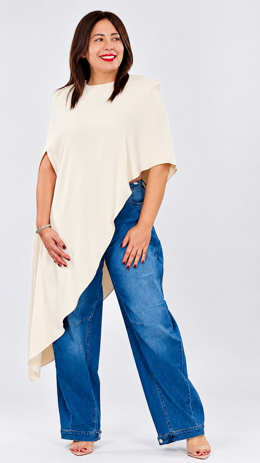 Blusa larga asimétrica de mujer color crema con hombreras, caída fluida y diseño tipo capa.
