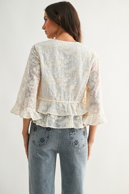 Lace Blouse color crema con bordado floral, lazos ajustables al frente y mangas amplias.