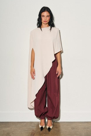 Blusa larga asimétrica de mujer color crema con hombreras, caída fluida y diseño tipo capa.