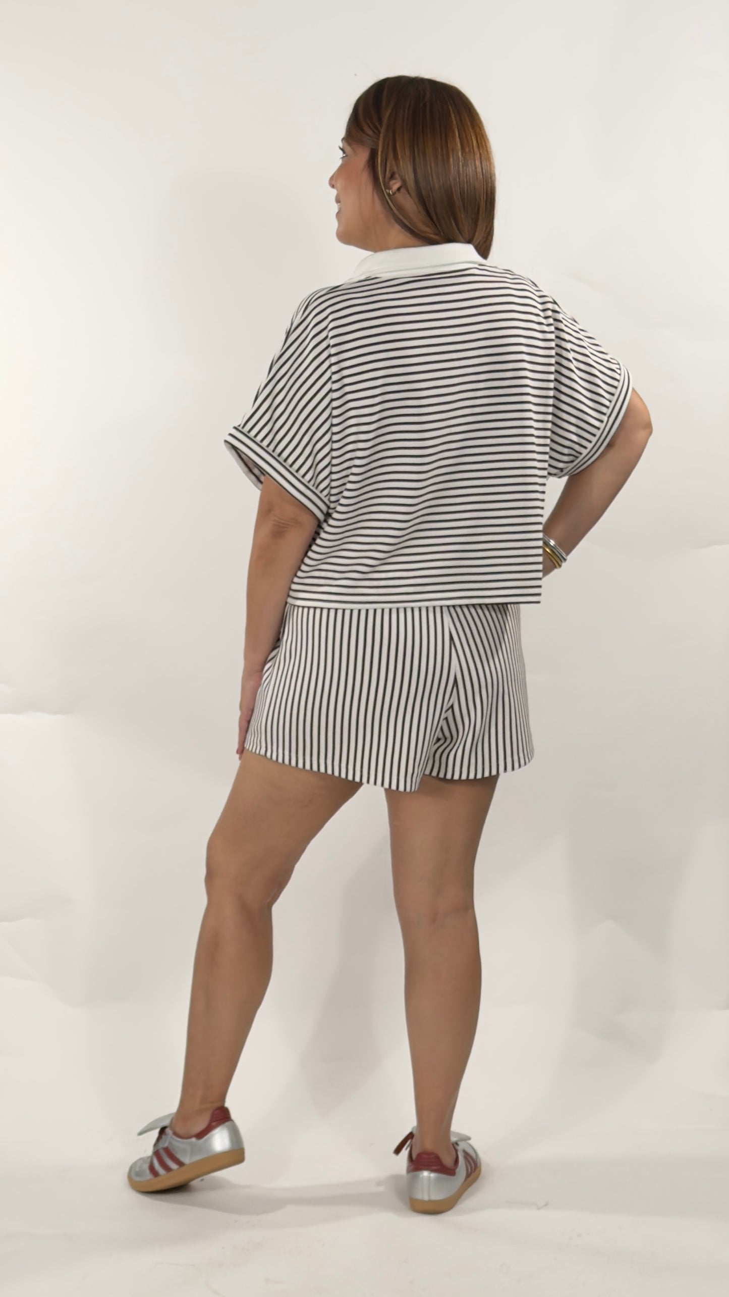 Conjunto de dos piezas a rayas negras con blusa suelta de cuello tipo polo y short con cordón en la cintura.