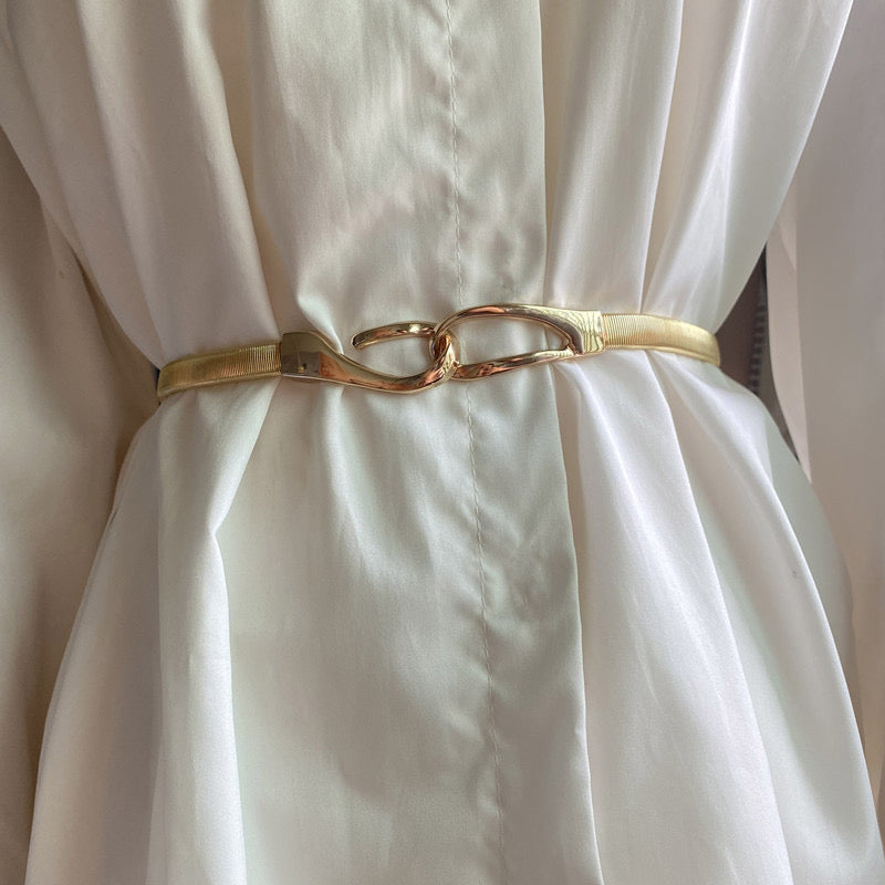 Correa elástica metálica con broche frontal tipo gancho, ideal para definir la cintura y complementar outfits elegantes o casuales.
