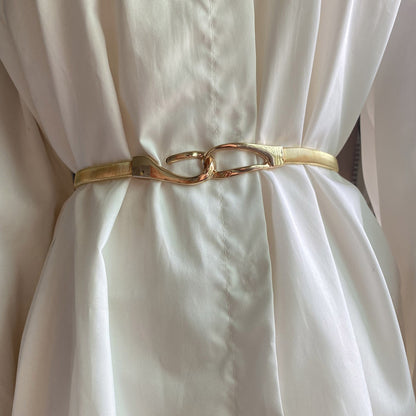 Correa elástica metálica con broche frontal tipo gancho, ideal para definir la cintura y complementar outfits elegantes o casuales.
