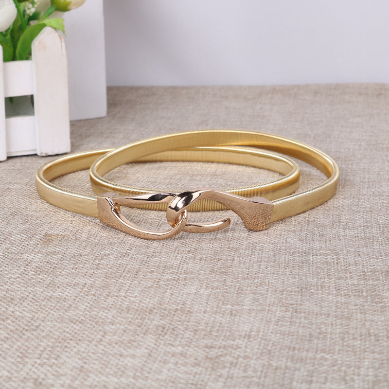 Correa elástica metálica con broche frontal tipo gancho, ideal para definir la cintura y complementar outfits elegantes o casuales.
