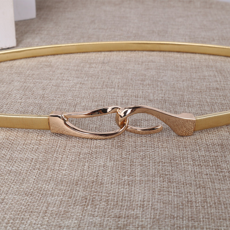 Correa elástica metálica con broche frontal tipo gancho, ideal para definir la cintura y complementar outfits elegantes o casuales.
